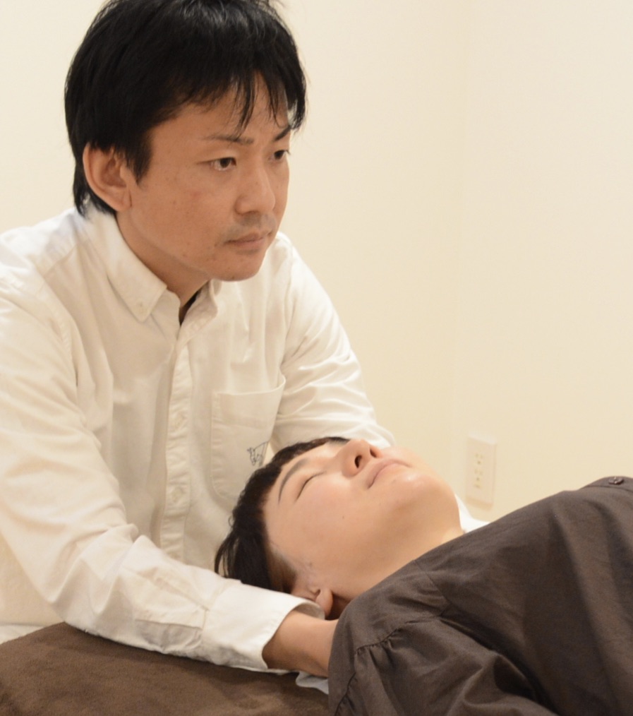 院長が来院者の首を優しく支えて施術している様子